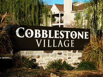 Cobblestone Village sign outside tan and white apartment complex