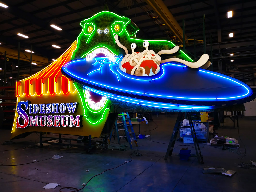 Large neon sign of dinosaur biting a flying saucer for Sideshow Museum