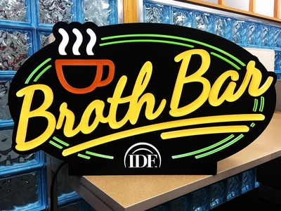 Neon Broth Bar circular sign with coffee cup above lettering